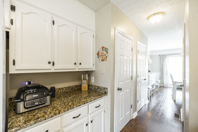 kitchen with dark wood-style floors, a textured ceiling, white cabinets, and dark stone countertops