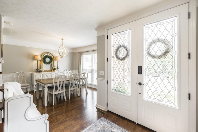 foyer entrance with dark wood finished floors, crown molding, visible vents, a textured ceiling, and a chandelier