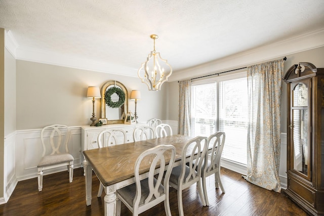 dining room featuring a textured ceiling, wainscoting, dark wood-style floors, an inviting chandelier, and crown molding