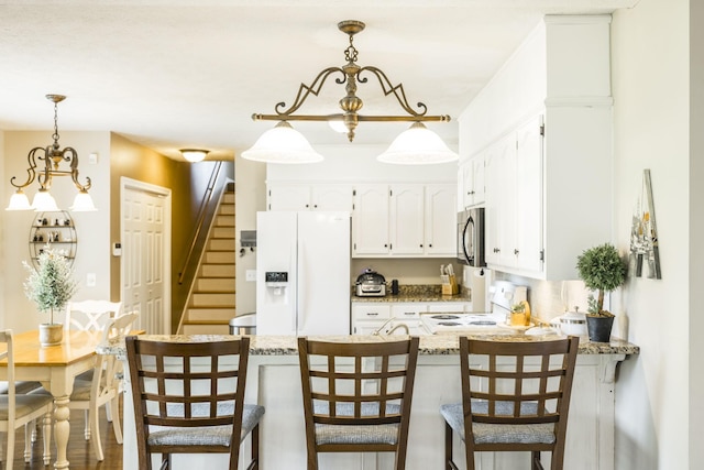 kitchen with white refrigerator with ice dispenser, stainless steel microwave, white cabinetry, range, and a peninsula