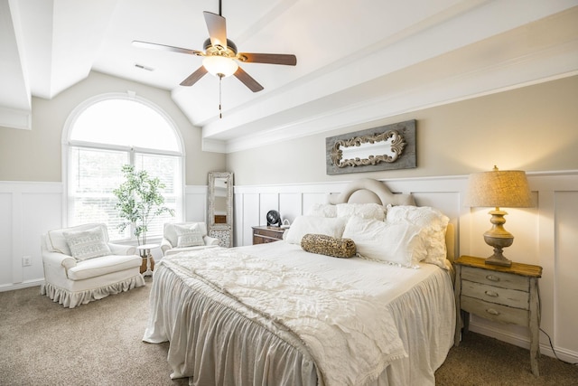 carpeted bedroom featuring a ceiling fan, a wainscoted wall, visible vents, and vaulted ceiling