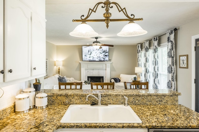 kitchen featuring a premium fireplace, a sink, white cabinetry, a ceiling fan, and open floor plan