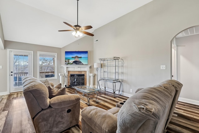 living room with arched walkways, a fireplace, wood finished floors, baseboards, and vaulted ceiling