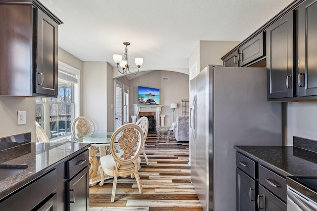 kitchen with a fireplace, dark stone countertops, wood finished floors, and a notable chandelier