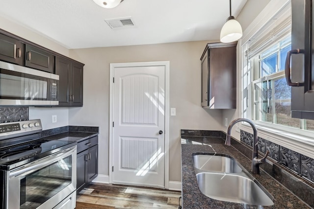 kitchen with dark brown cabinetry, a sink, visible vents, appliances with stainless steel finishes, and dark stone countertops