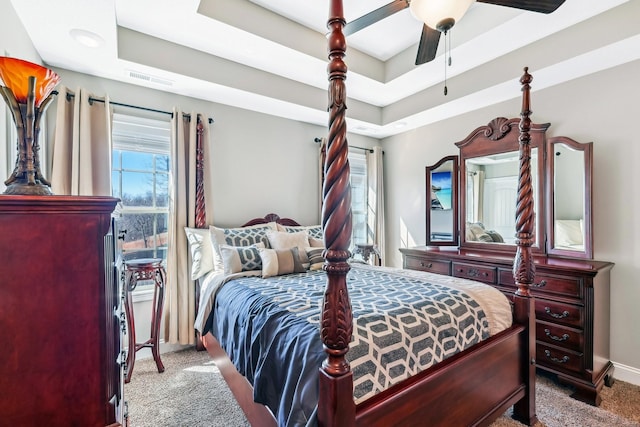 carpeted bedroom featuring multiple windows, a tray ceiling, and a ceiling fan