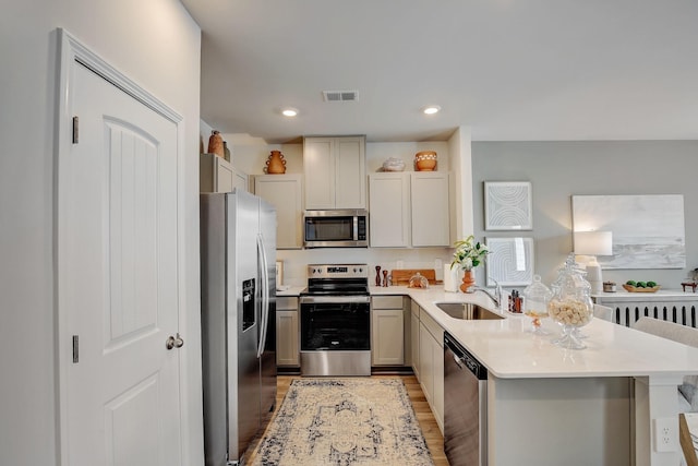 kitchen with a peninsula, a sink, visible vents, light countertops, and appliances with stainless steel finishes