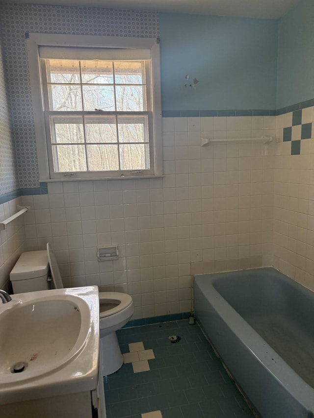 bathroom with wainscoting, toilet, a bath, tile patterned flooring, and tile walls