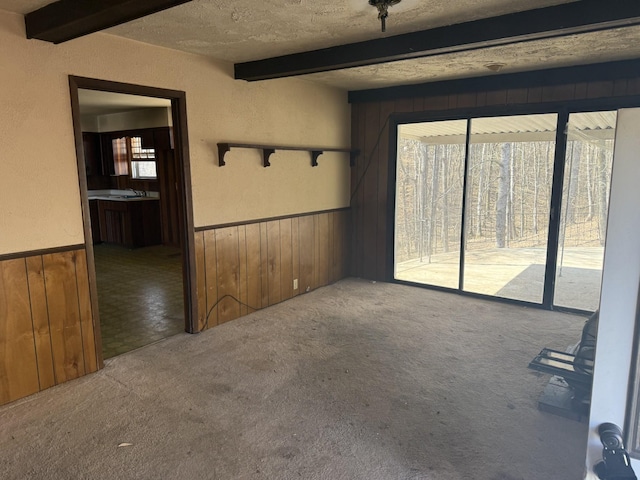 unfurnished room with carpet floors, beamed ceiling, and wood walls