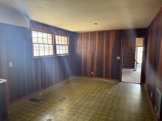 empty room featuring baseboards, wooden walls, and visible vents