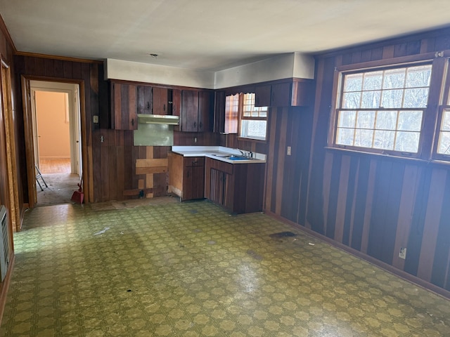 kitchen with under cabinet range hood, tile patterned floors, a sink, and wooden walls