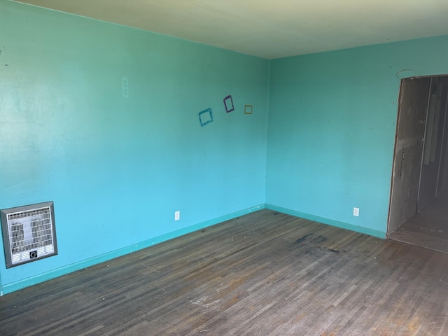 spare room with baseboards, heating unit, and wood finished floors