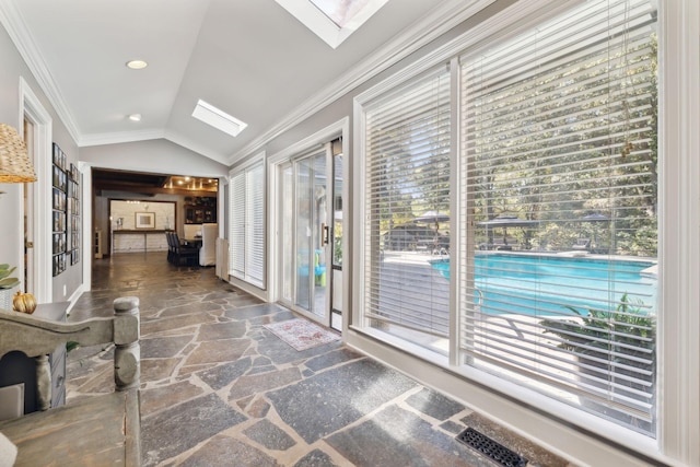 doorway to outside with plenty of natural light, vaulted ceiling with skylight, stone finish floor, and crown molding