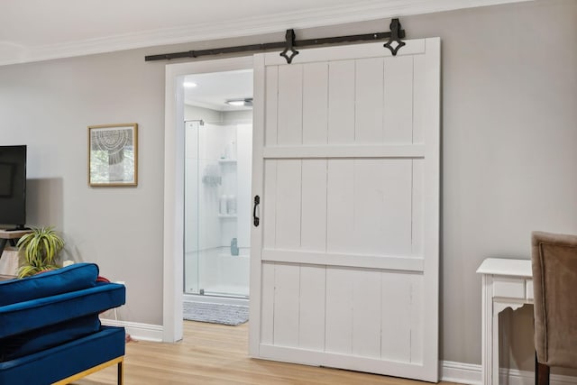 interior space with ornamental molding, a barn door, light wood-style flooring, and baseboards