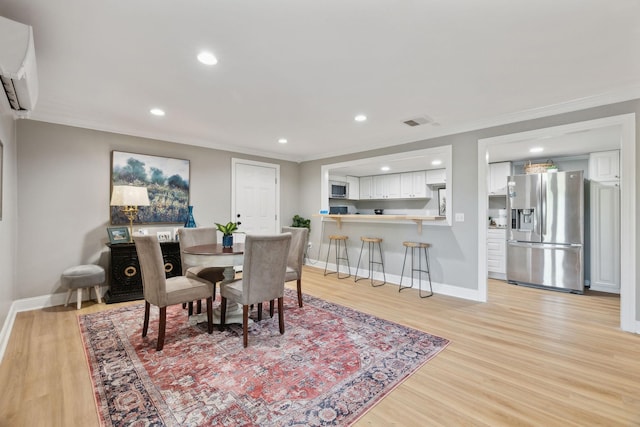 dining area featuring baseboards, light wood-type flooring, a wall unit AC, and crown molding