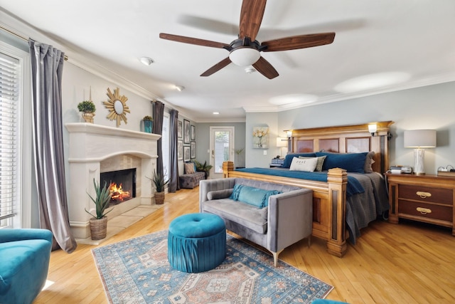 bedroom with light wood-type flooring, a premium fireplace, a ceiling fan, and crown molding