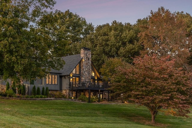 exterior space with stone siding, a chimney, a front yard, and a wooden deck