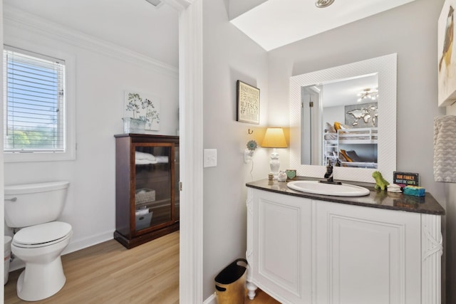 half bath featuring crown molding, toilet, vanity, wood finished floors, and baseboards