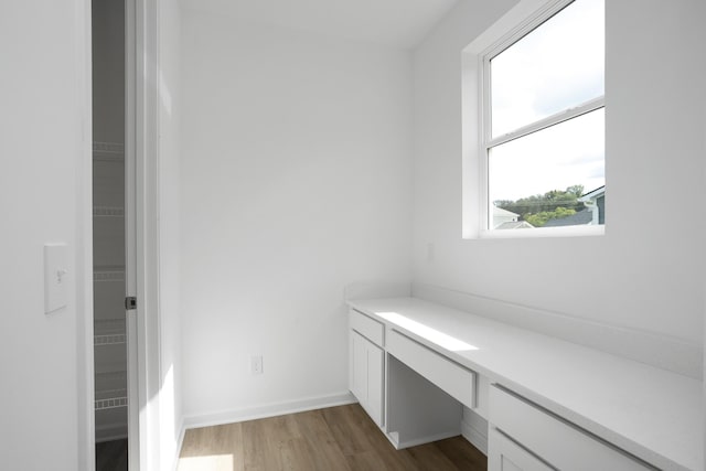 unfurnished office featuring light wood-type flooring, built in desk, and baseboards