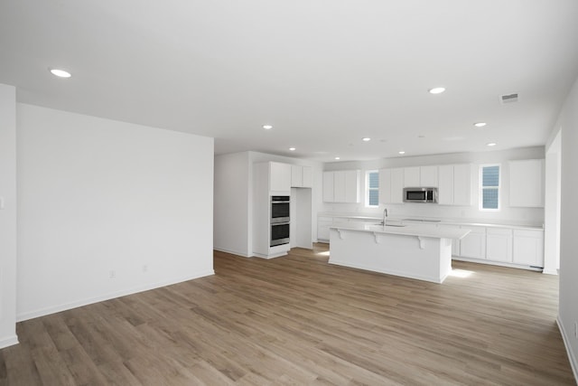 unfurnished living room featuring light wood-type flooring, visible vents, a sink, and recessed lighting