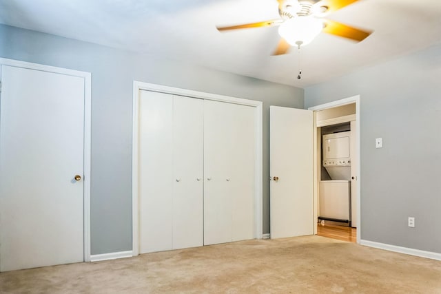 unfurnished bedroom featuring stacked washer and dryer, a closet, carpet flooring, and a ceiling fan