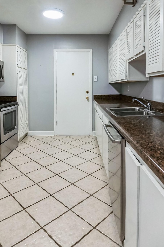 kitchen with light tile patterned floors, stainless steel appliances, dark countertops, white cabinetry, and a sink