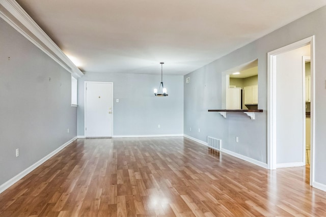 unfurnished living room featuring baseboards, wood finished floors, visible vents, and a notable chandelier