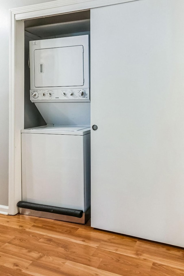 clothes washing area with laundry area, stacked washer / dryer, and light wood-style floors