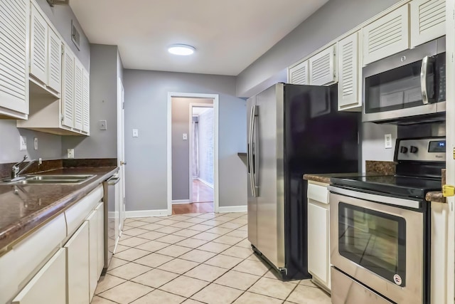 kitchen featuring light tile patterned floors, appliances with stainless steel finishes, dark countertops, and a sink