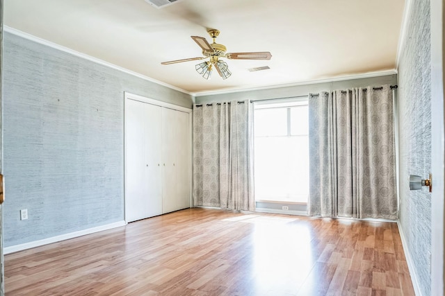 unfurnished bedroom featuring crown molding, a closet, visible vents, ceiling fan, and wood finished floors