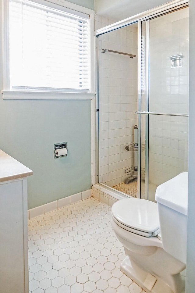 bathroom with toilet, a stall shower, and baseboards