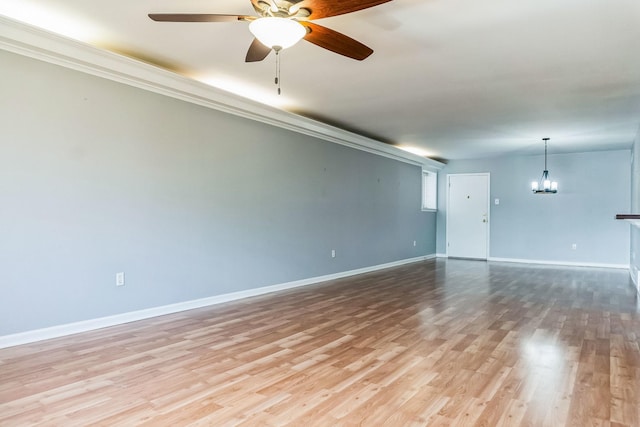 empty room featuring ceiling fan with notable chandelier, crown molding, wood finished floors, and baseboards