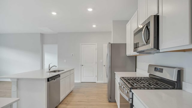 kitchen featuring light wood finished floors, appliances with stainless steel finishes, light countertops, white cabinetry, and a sink