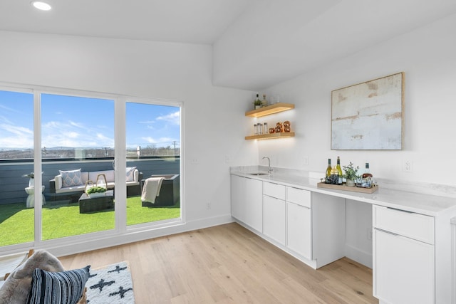 interior space featuring light countertops, light wood-style flooring, white cabinets, a sink, and baseboards