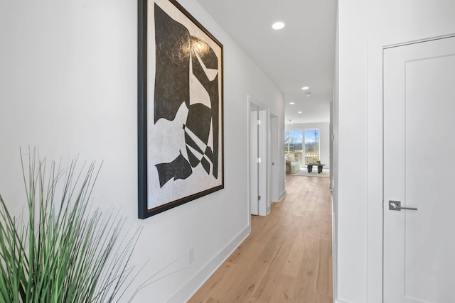 hall featuring baseboards, light wood-style flooring, and recessed lighting