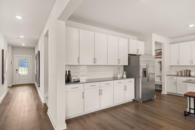 kitchen with dark countertops, dark wood-type flooring, white cabinetry, stainless steel refrigerator with ice dispenser, and backsplash