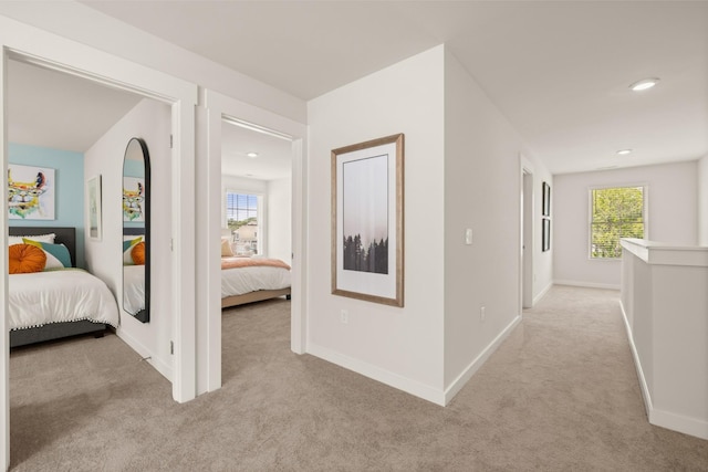 hall featuring a healthy amount of sunlight, light colored carpet, and baseboards