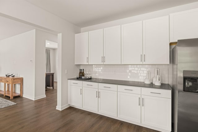 kitchen with dark wood-style floors, dark countertops, decorative backsplash, white cabinets, and stainless steel fridge