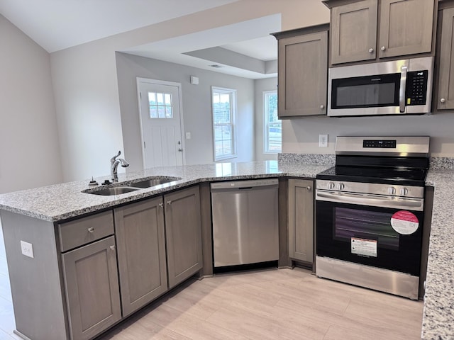 kitchen with appliances with stainless steel finishes, light stone counters, a peninsula, gray cabinetry, and a sink