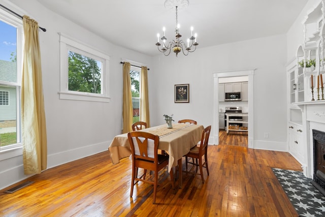 dining space with a notable chandelier, a fireplace with flush hearth, visible vents, baseboards, and hardwood / wood-style floors