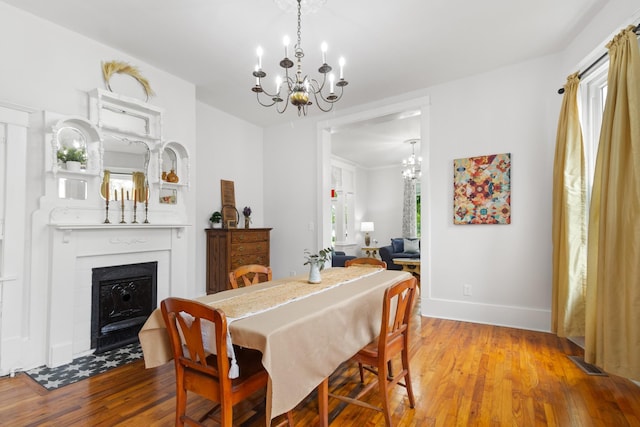 dining area with a fireplace, wood finished floors, visible vents, baseboards, and an inviting chandelier