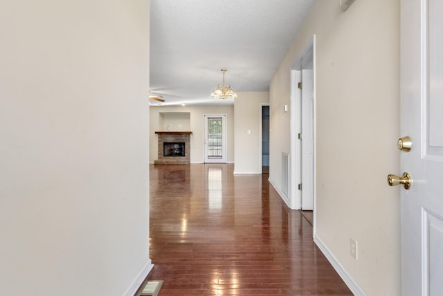 hallway with a textured ceiling, baseboards, a chandelier, and dark wood-style flooring