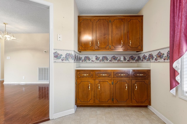 kitchen with a notable chandelier, light countertops, visible vents, brown cabinetry, and a textured ceiling