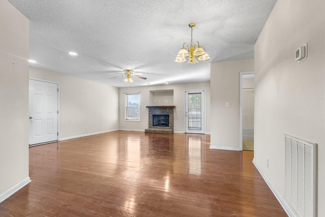 unfurnished living room with ceiling fan with notable chandelier, visible vents, hardwood / wood-style floors, and a stone fireplace