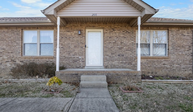 view of exterior entry with brick siding and roof with shingles