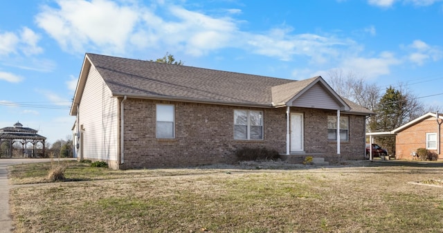 ranch-style home featuring a gazebo, roof with shingles, a front yard, and brick siding