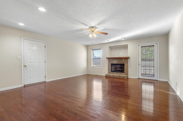 unfurnished living room with baseboards, ceiling fan, hardwood / wood-style floors, a textured ceiling, and a brick fireplace