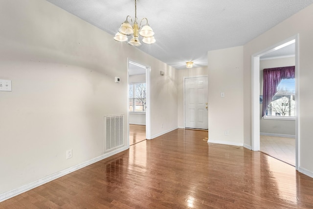 interior space featuring baseboards, visible vents, wood finished floors, a textured ceiling, and a notable chandelier