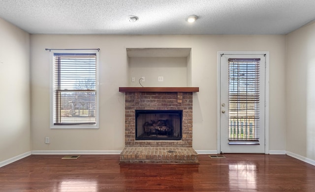 unfurnished living room with a brick fireplace, plenty of natural light, baseboards, and wood finished floors