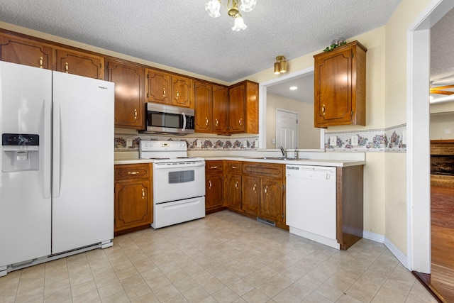 kitchen featuring white appliances, brown cabinets, light countertops, a textured ceiling, and a sink